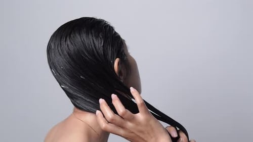 Back view of beautiful young Asian woman with long hair is applying conditioner on her hair.