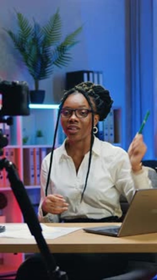 Pretty Woman Office Manager Sitting in Front of Videocamera in Workroom in Late Time and Holding