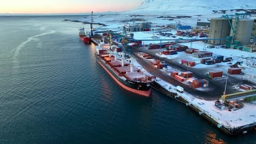 Container feeder and giant bulk carrier moored at a dock covered with snow in the iceland port Elkem