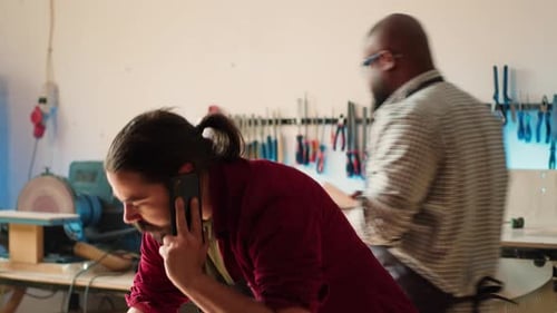 Un menuisier dans un atelier d'assemblage dessine des schémas en parlant sur un smartphone