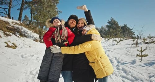 Happy Family Members Hug Tightly on Snowy Hill Near Forest