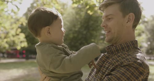 Father holding baby boy son in park in autumn on sunny day