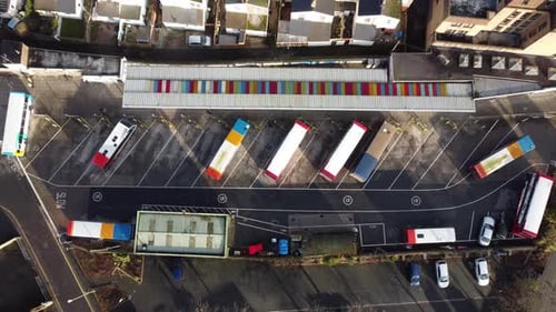 A slow rising, top down shot of a bus departing a bus station in a small colourful, city bus depot.