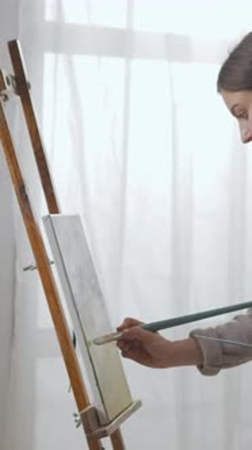 Focused Young Artist Painting on Canvas at Wooden Easel in Bright Minimalist Studio Carefully