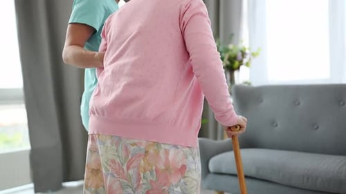 Caregiver assists Senior Woman to Sit on Sofa