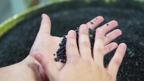 Hands handling small pieces of plastic to be melted for recycling.