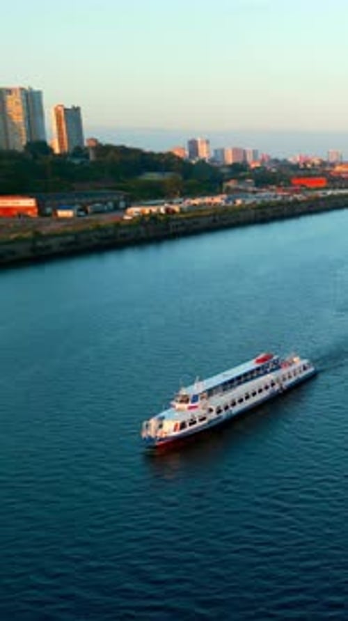 Passenger Ferry Navigating River at Sunrise Near City Coastline Clip