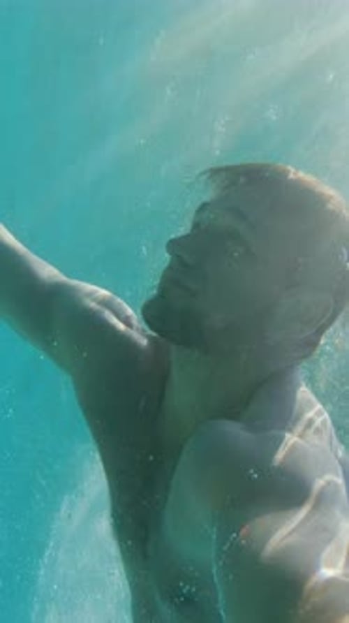 Schöner junger Mann schwimmt im warmen, sonnigen Sommer unter der Wasseroberfläche im türkisblauen Meer