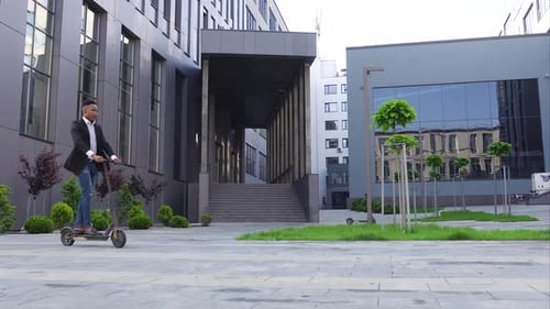 African american man in trendy wear riding on e-scooter near beautiful city buildings