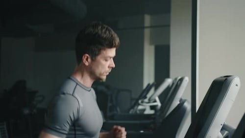 Medium Close Up Profile Shot of Handsome Man Running on Treadmill in Gym