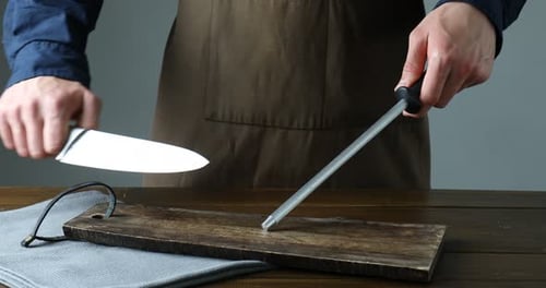 Man sharpening knife with sharpener at wooden table against grey background, closeup
