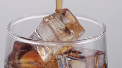 Close Up Of Fresh Cola Being Poured In To The Glass With Ice Cubes On White Background