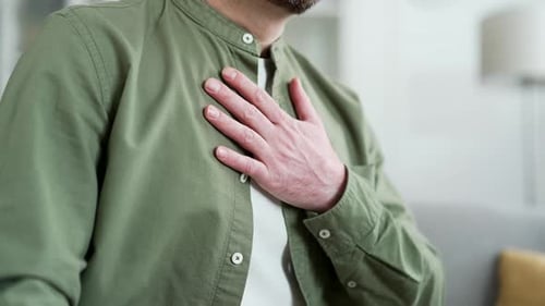 Close up. Male hands holding massaging chest. Mature man in green shirt has heart attack while