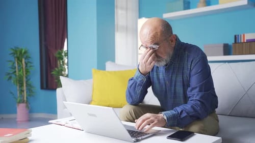 Tired Man Using Laptop at Home on Couch