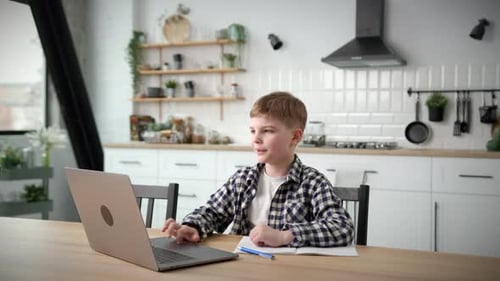 School Boy Studying Online Using Laptop at Home Kid Writing in Notebook and Listening to Online