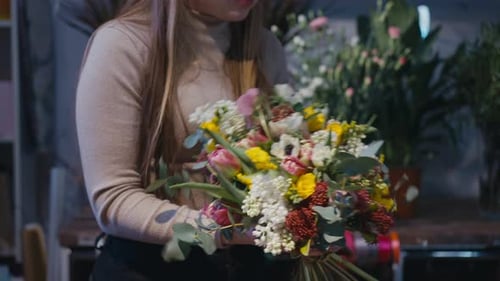 Une fleuriste méconnaissable coupant des tiges de fleurs et étirant un bouquet devant la caméra, heureuse et souriante