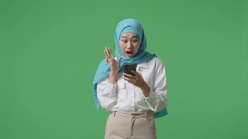 Asian Muslim Woman Looking At Smartphone And Saying Wow While Standing In The Green Screen