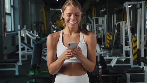 Sportswoman Smiles Reading Messages in Wellequipped Gym