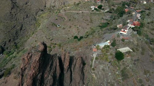 Aerial Tilt Downward Revealing Mountainside Village by Pointed Rock Formation, Daytime