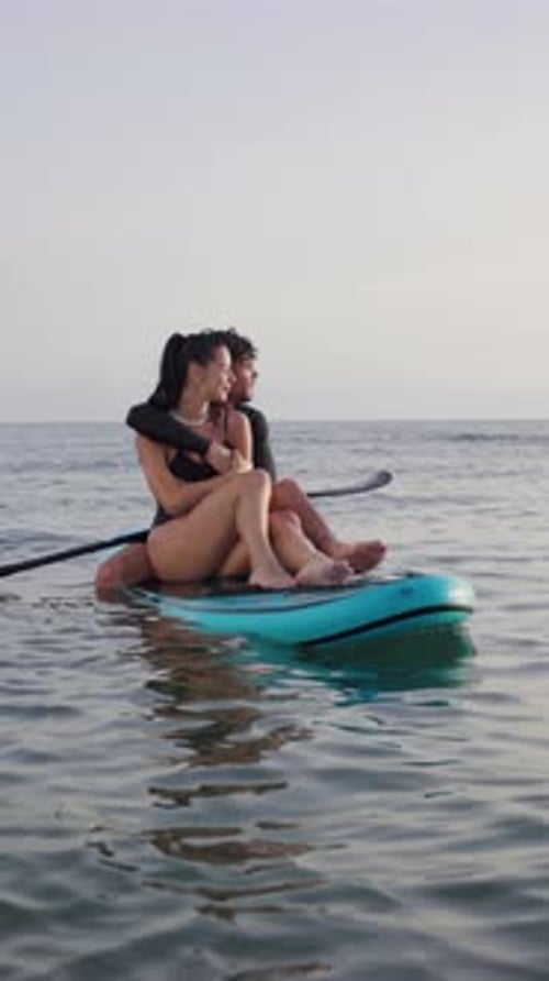 Romantic couple embracing on stand up paddle board at sunset