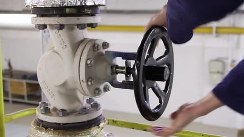Worker Turning Valve Wheel on Industrial Pipe