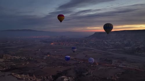 Drone view of dozens of balloons taking off at twilight, illuminated by burner flames in Rose Valley