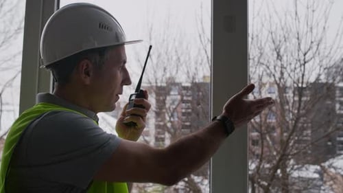 Foreman Using Walki-Talkie while Instructing by Window in Construction Office