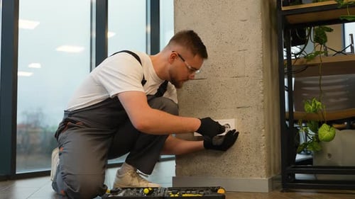 Electrician Kneeling Repairing Outlet in Modern Office