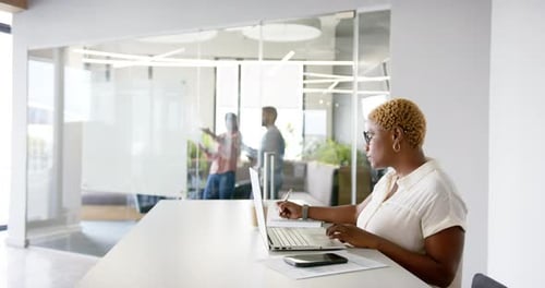 Working in modern office, woman using laptop and writing notes at desk, copy space
