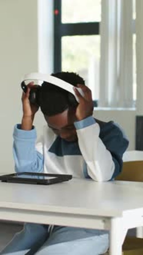 Vertical video: Reaching child in blue top putting on headphones at home, tapping tablet for help