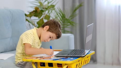 Boy Drawing at Table with Laptop Computer