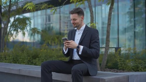 Businessman Holding Phone Reading Email Sits on Street Smiling Writes Message Communicates in Social