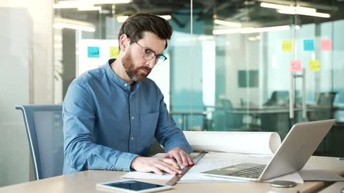 Bearded Man Designs with Laptop in Modern Office