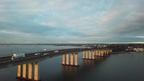 Aerial: Drone shot slowly rising to reveal traffic driving over a large bridge whilst commuting to w