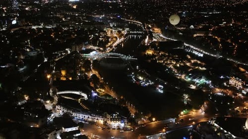 Aerial timelapse of downtown Tbilisi, Georgia at night with traffic and hot air balloon and lights.