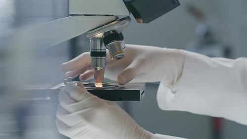 Mains d'un scientifique ajustant la lame sur la platine du microscope en laboratoire