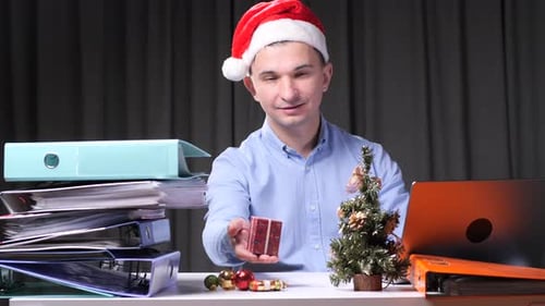 Office Worker Wearing Santa Hat Offering Christmas Gift at Workplace