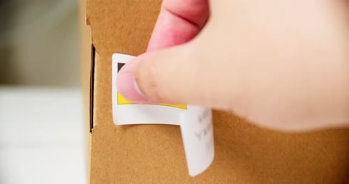 Hands applying MADE IN GERMANY flag label on a shipping cardboard box with products. Close up shot w