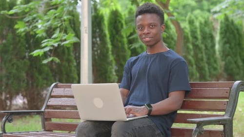 Casual African Man Smiling with Laptop in Park
