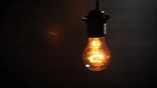 Hanging on Wire Incandescent Bulb Turns On and Off Flickers on Black Background