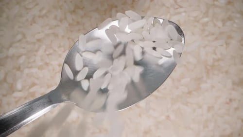 Weißer Reis wird von oben auf einen Löffel gegossen, ein rotierender Hintergrund aus Körnern von unten.
Zeitlupe