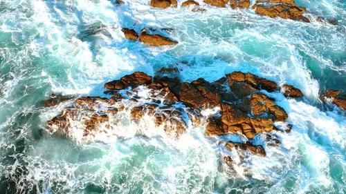 Bare rock sticking out of water. White foamy waves splash by the rock. Beautiful ocean at the shore