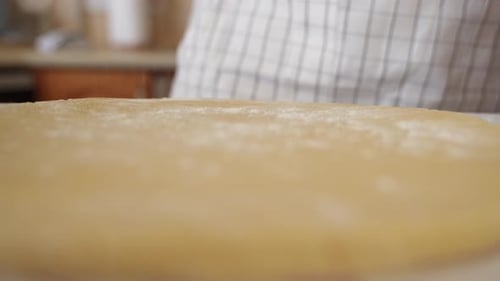 A baker sprinkles flour on pastry dough, close-up low angle view.