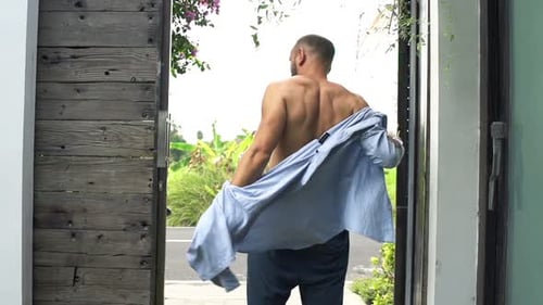 Man Putting on Shirt Standing by Door in Country, Super
