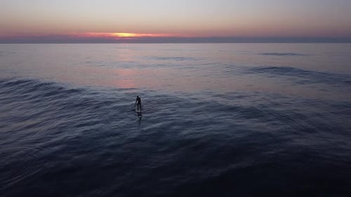 Silhouette of surfer on inflatable SUP, paddling at amazing sunset over water, Aerial view