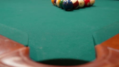 Pool Balls are Broken on an 8 Ball Triangle Rack and the Purple Stripe 12 Ball Slowly Rolls towards