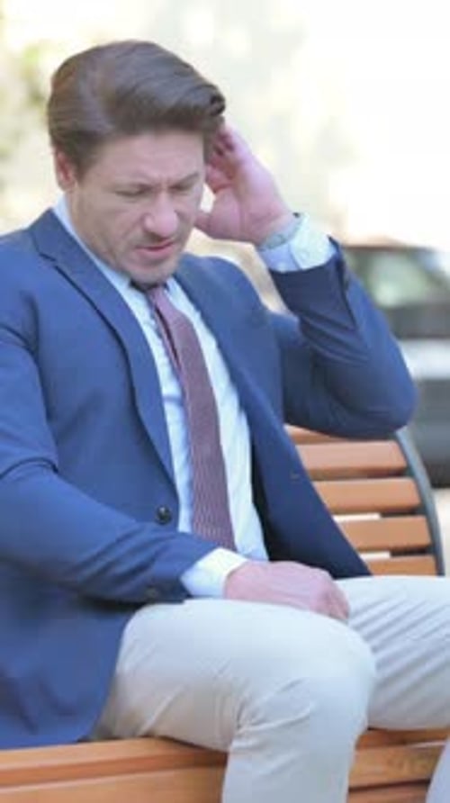 Man in suit sitting outside, looking stressed