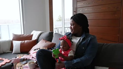 Woman with infant on the couch playing with toy