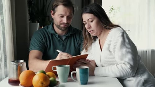 Couple Reviewing Notebook Together at Table Indoors