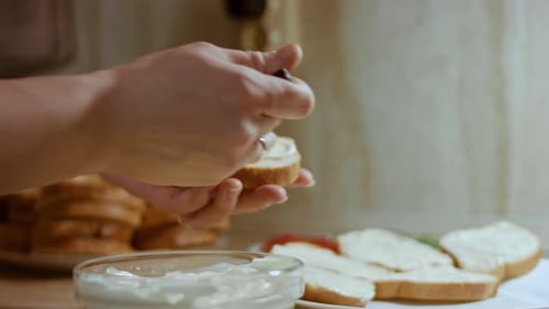 Woman Spreads Cream Cheese on Bread in Kitchen